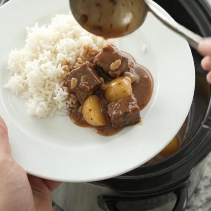 Slow cooker bourbon gravy beef bites with potatoes and garlic, served in a black crockpot