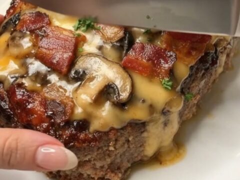 A beautifully sliced cheesy bacon and mushroom meatloaf on a white platter with visible layers of melted cheddar.