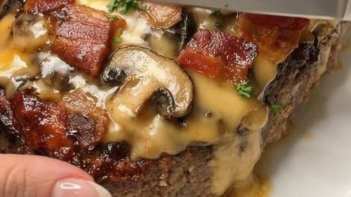 A beautifully sliced cheesy bacon and mushroom meatloaf on a white platter with visible layers of melted cheddar.