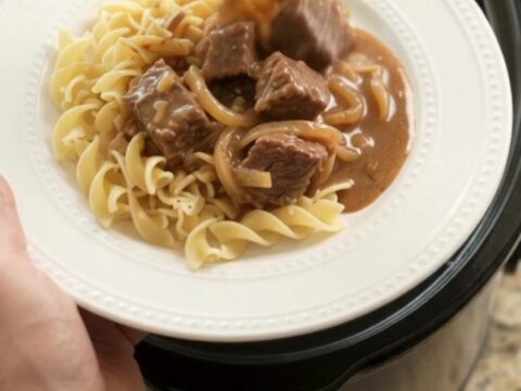 Slow cooker filled with tender beef and onions in a rich sour cream gravy, steam rising.
