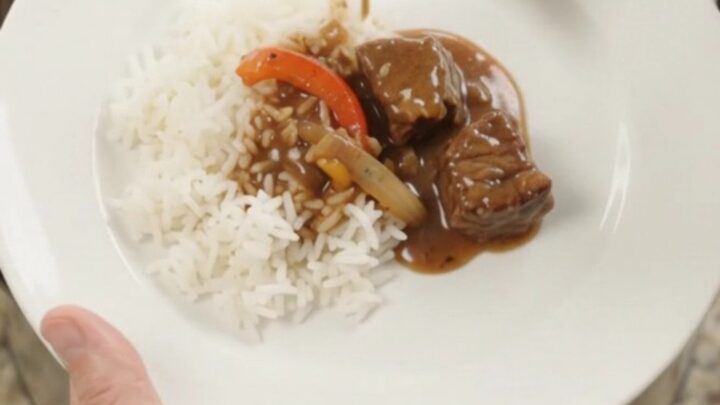 Slow cooker filled with bourbon gravy beef bites, peppers, and onions