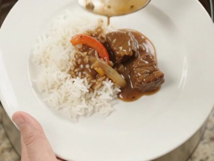 Slow cooker filled with bourbon gravy beef bites, peppers, and onions