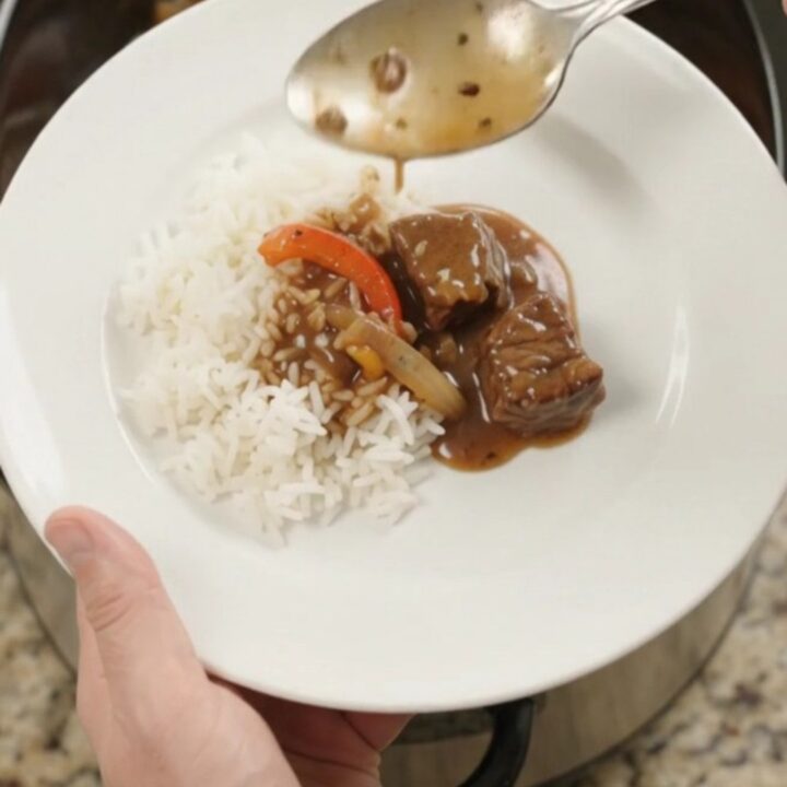 Slow cooker filled with bourbon gravy beef bites, peppers, and onions