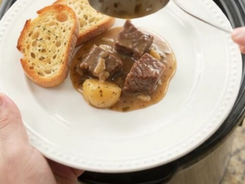Slow cooker beef and potatoes in a creamy Gruyère sauce, served on a white plate with brioche