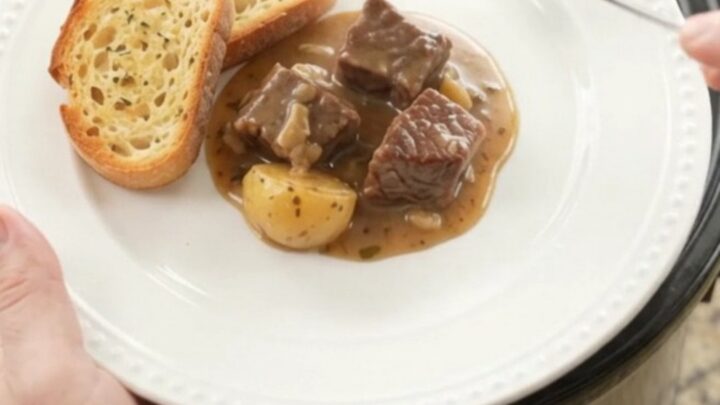 Slow cooker beef and potatoes in a creamy Gruyère sauce, served on a white plate with brioche