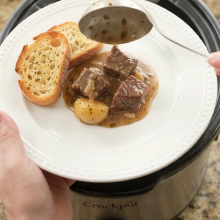 Slow cooker beef and potatoes in a creamy Gruyère sauce, served on a white plate with brioche