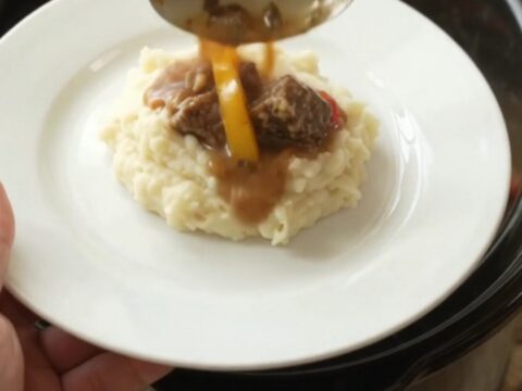 Slow cooker filled with tender beef bites, bell peppers, and onions in a golden butter au jus.