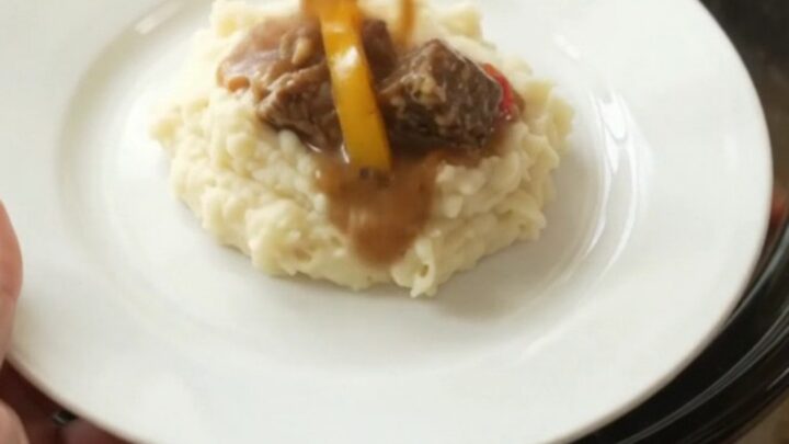 Slow cooker filled with tender beef bites, bell peppers, and onions in a golden butter au jus.