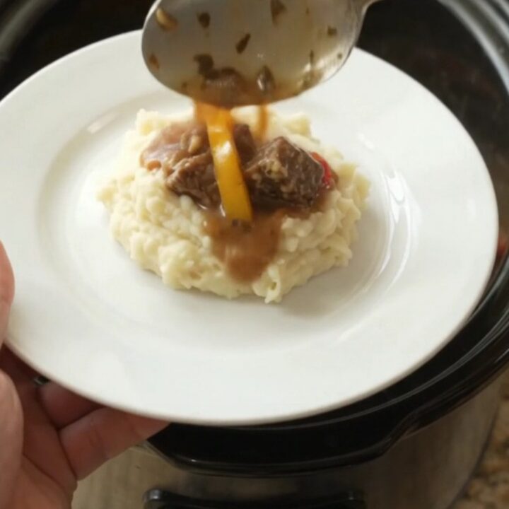 Slow cooker filled with tender beef bites, bell peppers, and onions in a golden butter au jus.