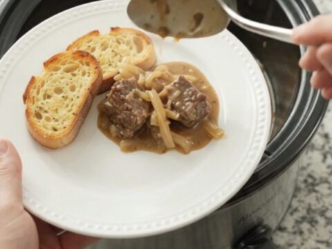 Slow-cooker French onion beef with Gruyère sauce in a black crockpot, garnished with thyme