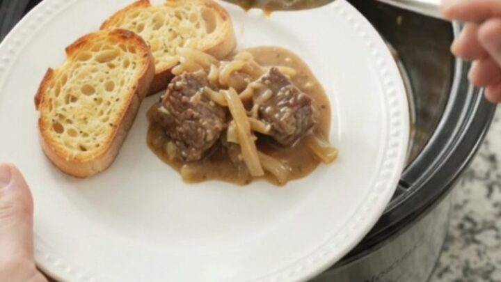 Slow-cooker French onion beef with Gruyère sauce in a black crockpot, garnished with thyme