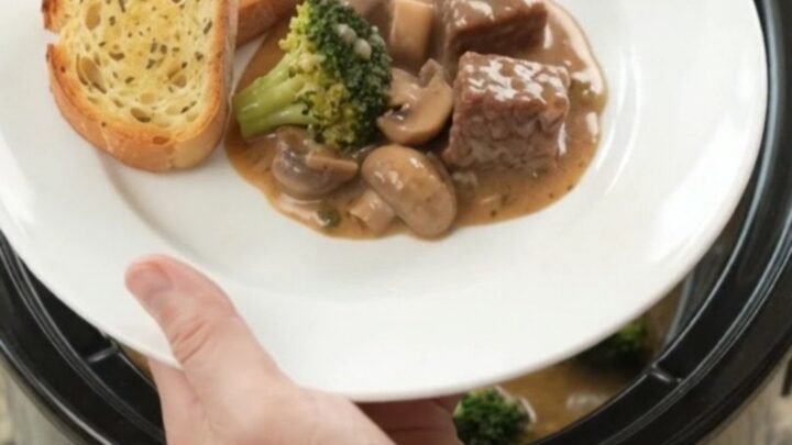 Slow cooker filled with creamy Gruyère sauce, beef, broccoli, and mushrooms