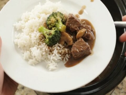Crockpot Bourbon Gravy Broccoli Beef Bites in a black slow cooker, with steam rising