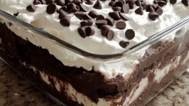 A square glass dish filled with layers of crushed Oreo cookies, chocolate pudding, and whipped cream