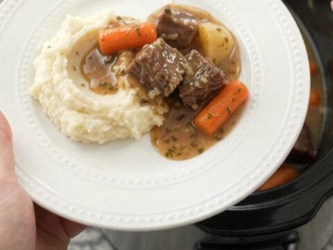 Slow cooker filled with tender beef, carrots, and potatoes in a golden sauce