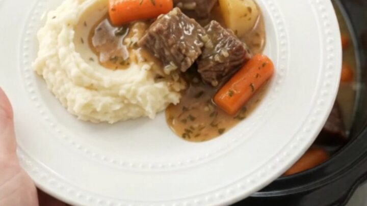 Slow cooker filled with tender beef, carrots, and potatoes in a golden sauce