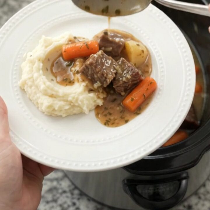 Slow cooker filled with tender beef, carrots, and potatoes in a golden sauce