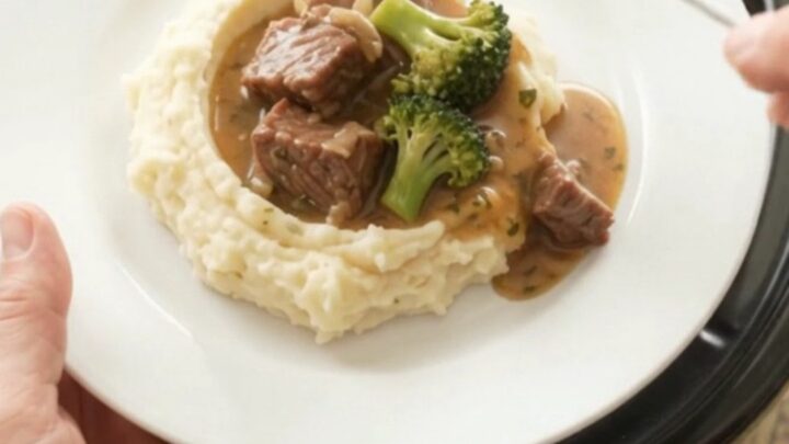 Slow cooker cowboy butter broccoli beef bites bubbling in the crockpot with a spoon lifting a scoop