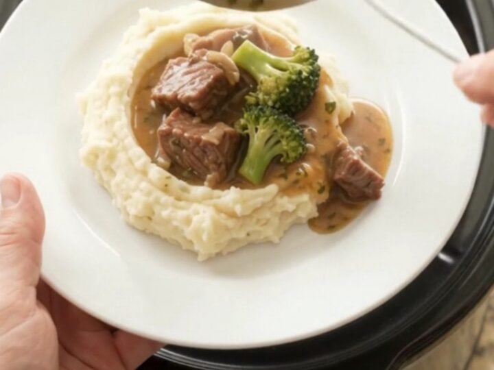 Slow cooker cowboy butter broccoli beef bites bubbling in the crockpot with a spoon lifting a scoop