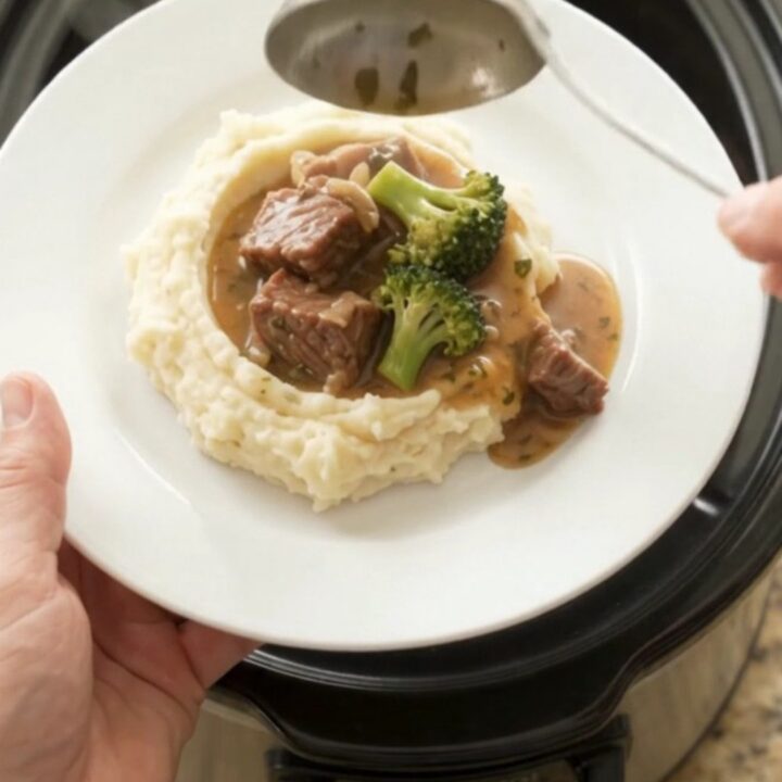 Slow cooker cowboy butter broccoli beef bites bubbling in the crockpot with a spoon lifting a scoop