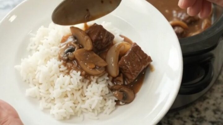 Slow cooker full of tender beef, portobello mushrooms, and shallots in a glossy bourbon gravy