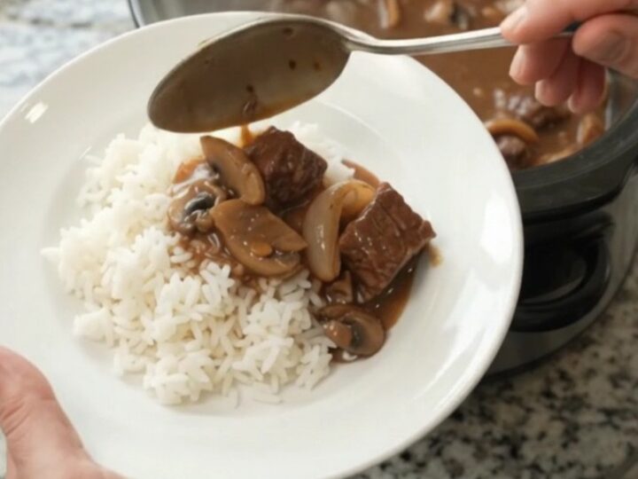 Slow cooker full of tender beef, portobello mushrooms, and shallots in a glossy bourbon gravy