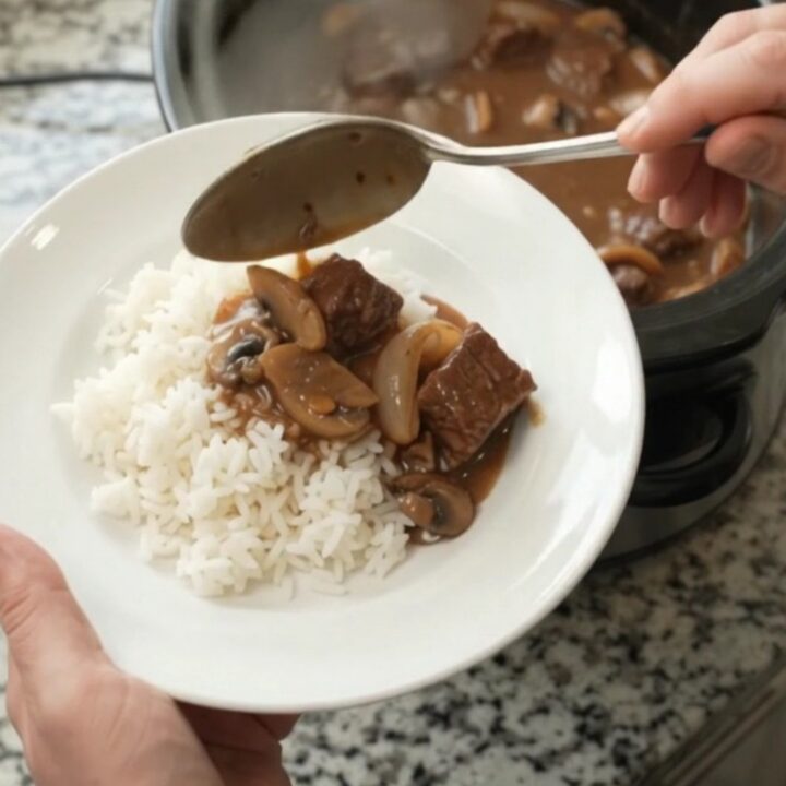 Slow cooker full of tender beef, portobello mushrooms, and shallots in a glossy bourbon gravy