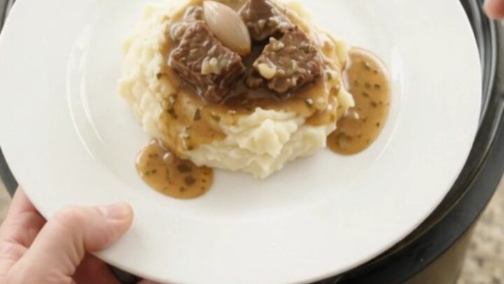 Bubbling slow cooker beef bites with mushrooms and shallots in a garlic-herb butter au jus, topped with fresh herbs.