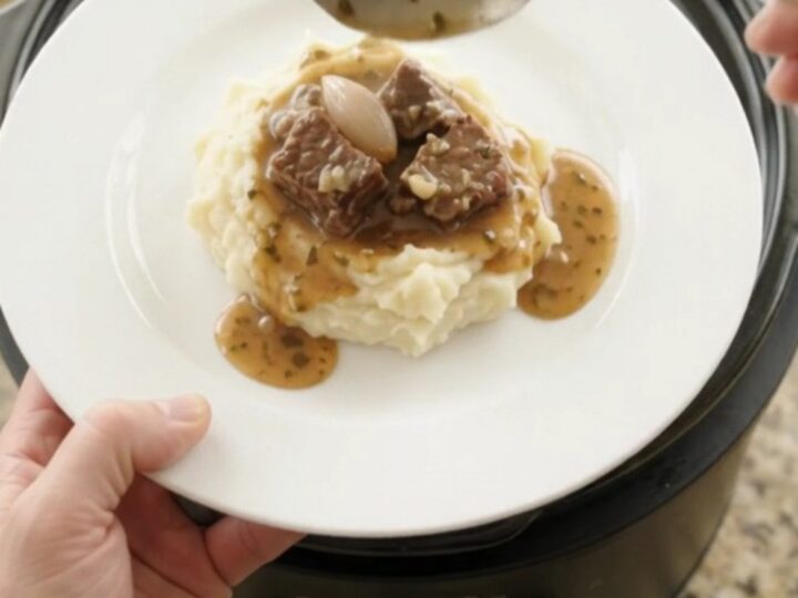 Bubbling slow cooker beef bites with mushrooms and shallots in a garlic-herb butter au jus, topped with fresh herbs.