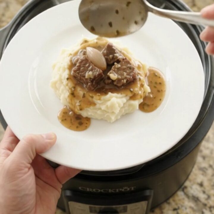 Bubbling slow cooker beef bites with mushrooms and shallots in a garlic-herb butter au jus, topped with fresh herbs.