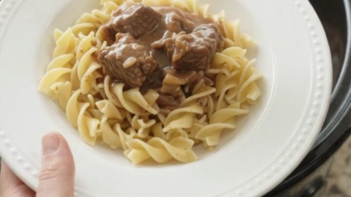 A slow cooker filled with tender beef, portobello mushrooms, and shallots in a rich sour cream gravy.