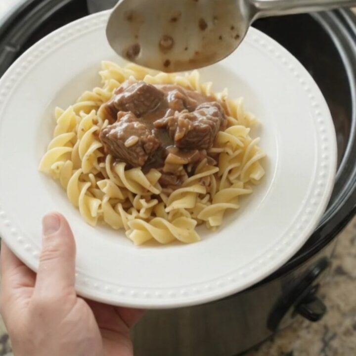 A slow cooker filled with tender beef, portobello mushrooms, and shallots in a rich sour cream gravy.