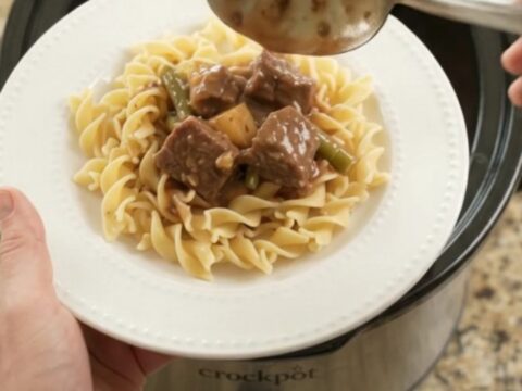 Slow cooker filled with beef, green beans, and potatoes in a rich brown gravy, seen from above.