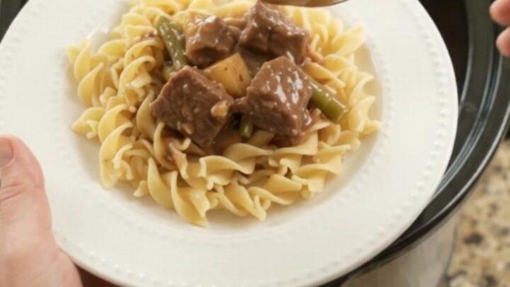 Slow cooker filled with beef, green beans, and potatoes in a rich brown gravy, seen from above.