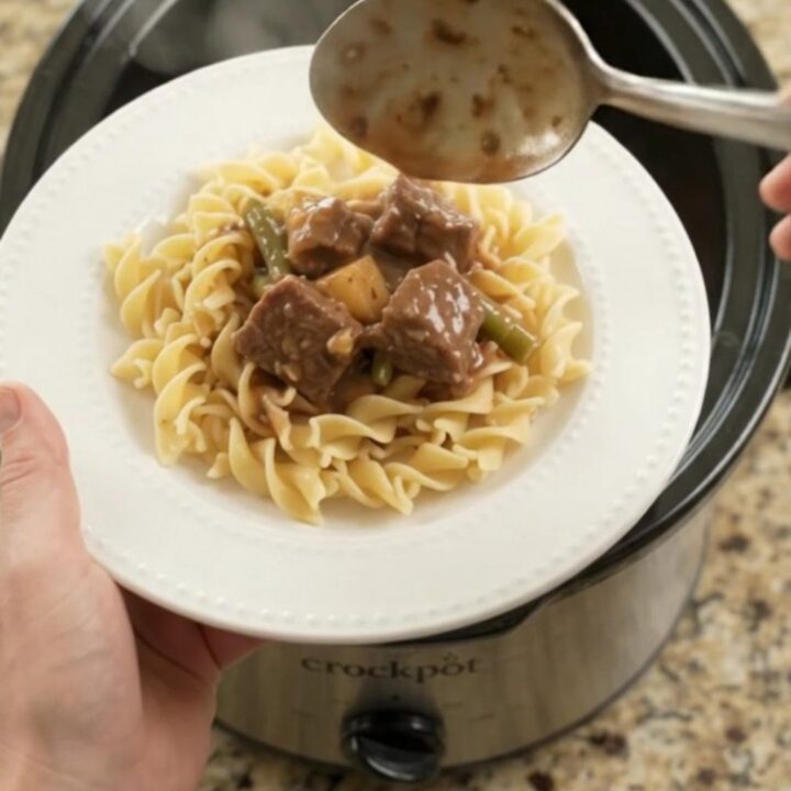Slow cooker filled with beef, green beans, and potatoes in a rich brown gravy, seen from above.