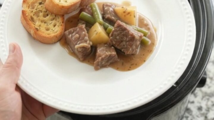 Slow cooker filled with creamy beef, green beans, and potatoes in a rich cheese sauce