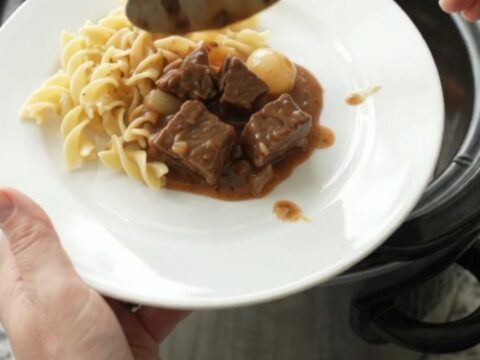 Slow cooker beef bites with pearl onions and carrots in creamy gravy, served in a black Crockpot