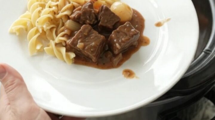 Slow cooker beef bites with pearl onions and carrots in creamy gravy, served in a black Crockpot