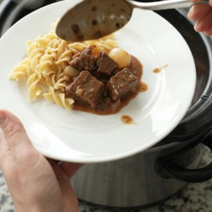 Slow cooker beef bites with pearl onions and carrots in creamy gravy, served in a black Crockpot