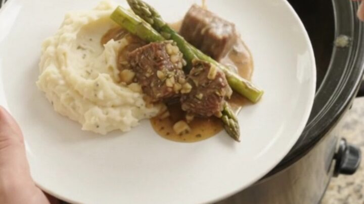 Slow cooker cowboy butter asparagus beef bites in a black crockpot, with steam rising