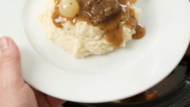 Slow cooker beef bites with pearl onions and carrots in a glossy butter au jus, topped with a spoonful of sauce.