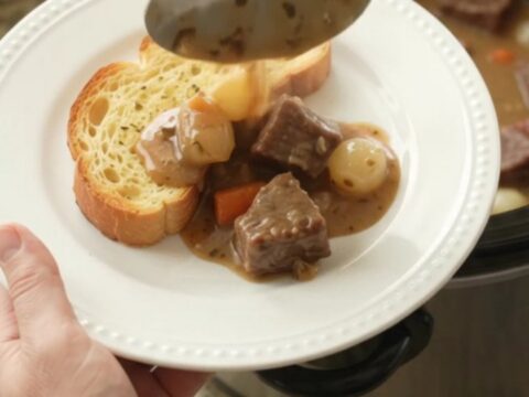 A slow cooker filled with tender beef chunks, pearl onions, and carrots in a creamy Gruyère sauce