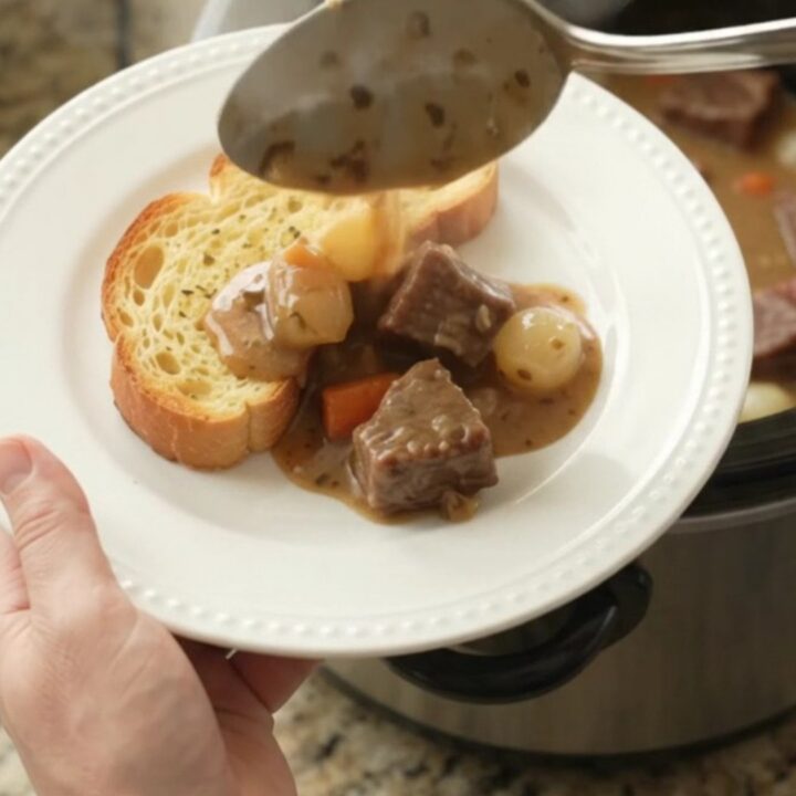 A slow cooker filled with tender beef chunks, pearl onions, and carrots in a creamy Gruyère sauce