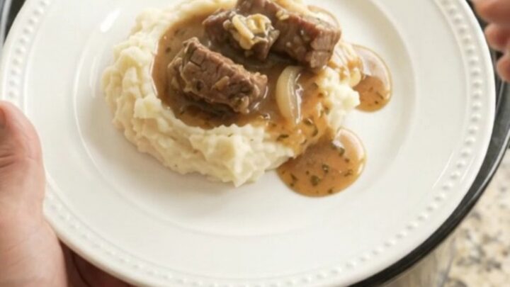 Slow cooker cowboy butter pepper sirloin tips in a black crockpot with steam rising