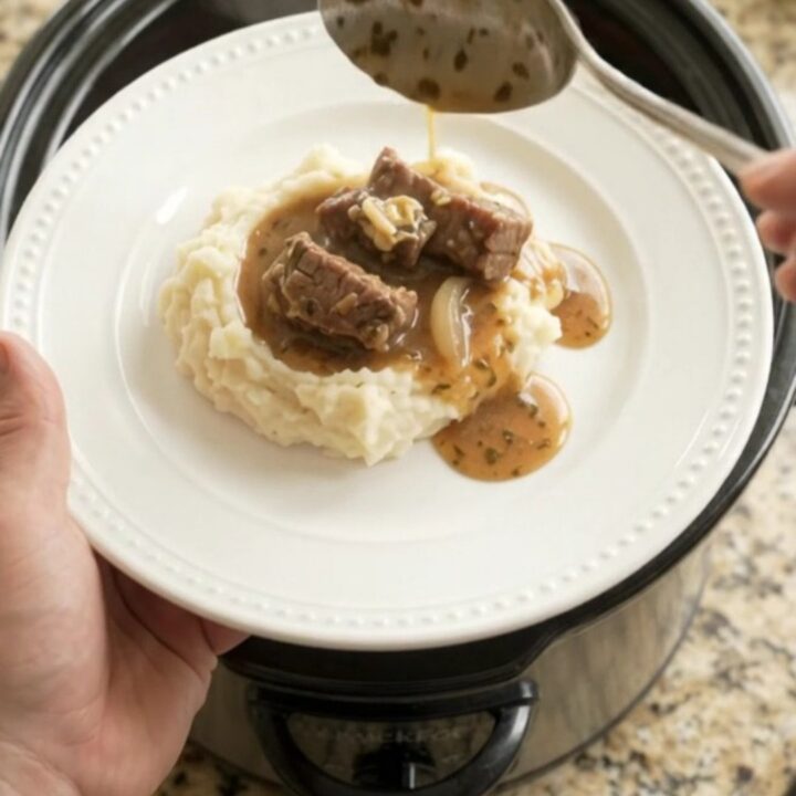 Slow cooker cowboy butter pepper sirloin tips in a black crockpot with steam rising