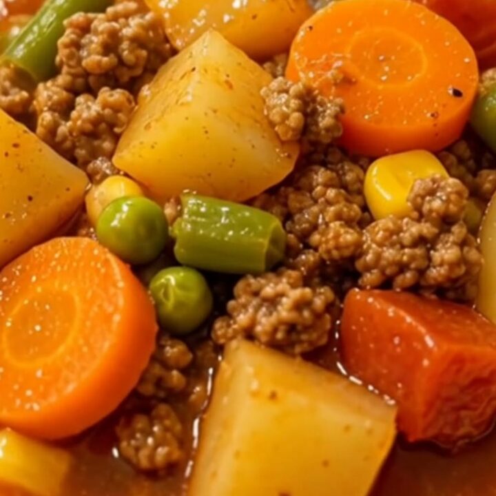 A steaming bowl of vegetable beef soup featuring carrots, potatoes, and ground beef in a rich, glossy broth.
