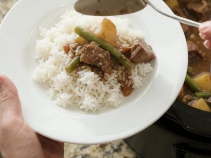 Slow cooker sirloin tips with green beans and potatoes in bourbon gravy, served in a black crockpot.