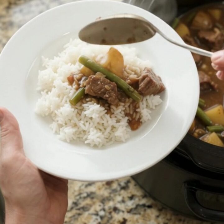 Slow cooker sirloin tips with green beans and potatoes in bourbon gravy, served in a black crockpot.