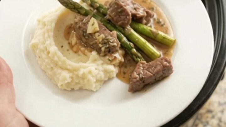 Slow cooker filled with tender sirloin tips and asparagus in a golden garlic-herb butter sauce
