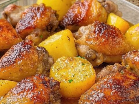 A golden, crispy chicken thigh and roasted potato wedge in a glass dish with herb garnish.